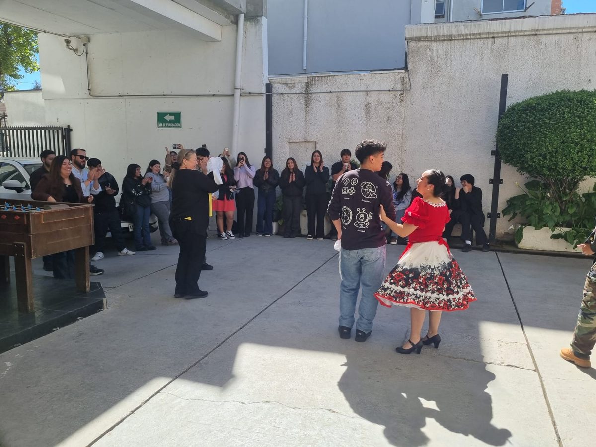 El estudiante Eduardo Navarrete baila cueca junto a una integrante del conjunto folclórico, rodeado por el público